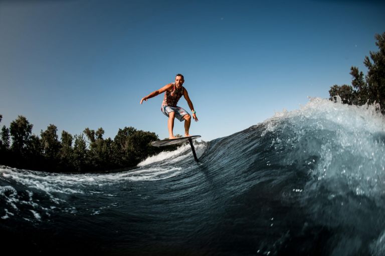 adult sportive man skillfully riding on the wave with hydrofoil foilboard on background of blue sky
