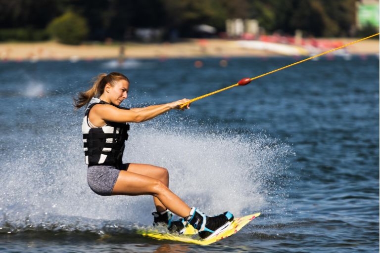 Female wakeboarder wakesurfing. Girl riding waterski cabel. Holding tow rope. Summer activities in the lake.
